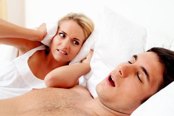 Woman angry that her husband is snoring loudly. She's covering her ears with the pillow.